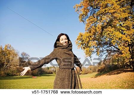 Stock Photo - Portrait of a brunette beautiful woman with arms opened in park in Autumn. Fotosearch