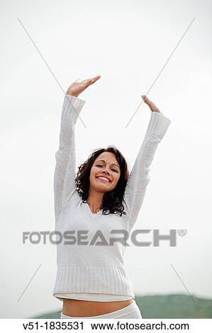 Stock Image - Portrait of a brunette woman breathing fresh air by the sea smiling at camera. Fotosearch