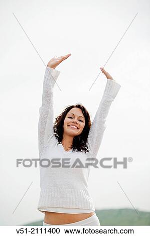 Stock Image - Portrait of a brunette woman breathing fresh air by the sea smiling at camera. Fotosearch
