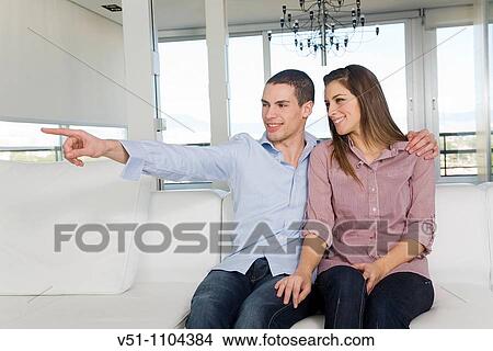 Portrait of a couple sitting on the sofa, he is pointing the horizon View Large Photo Image Picture - Portrait of a couple sitting on the sofa, he is pointing the horizon. Fotosearch