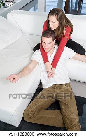 Stock Image - Portrait of a couple sitting on the sofa, he is pointing the horizon. Fotosearch