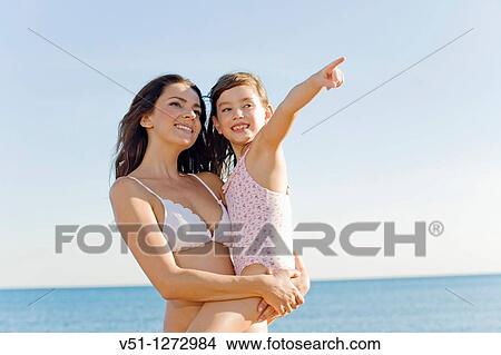 Portrait of a cute daughter pointing away with mother at the beach View Large Photo Image Picture - Portrait of a cute daughter pointing away with mother at the beach. Fotosearch