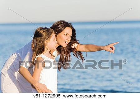 Portrait of a cute woman pointing away with daughter at the beach View Large Photo Image Stock Photography - Portrait of a cute woman pointing away with daughter at the beach. Fotosearch