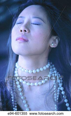 Stock Photography - Portrait of a glamorous young Chinese woman, face tilted up to the left with eyes closed and wearing a long pearl necklace. Fotosearch