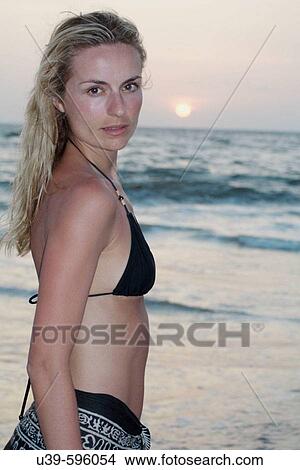 Portrait of a good looking blonde woman next to the ocean in a black bikini and sarong looking at camera with the sun setting. View Large Photo Image Picture - Portrait of a good looking blonde woman next to the ocean in a black bikini and sarong looking at camera with the sun setting.. Fotosearch