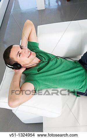 Portrait of a man lying on the sofa listening to music with headphones View Large Photo Image Picture - Portrait of a man lying on the sofa listening to music with headphones. Fotosearch