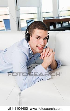 Portrait of a man lying on the sofa listening to music with headphones View Large Photo Image Stock Image - Portrait of a man lying on the sofa listening to music with headphones. Fotosearch