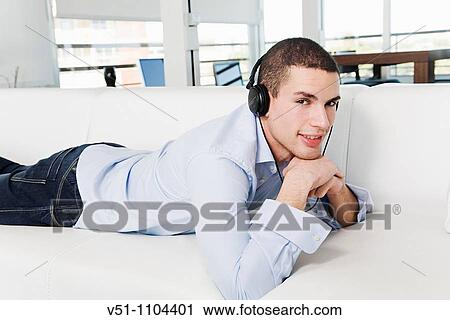 Portrait of a man lying on the sofa listening to music with headphones View Large Photo Image Stock Image - Portrait of a man lying on the sofa listening to music with headphones. Fotosearch