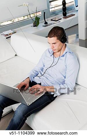 Portrait of a man lying on the sofa listening to music with headphones and using laptop View Large Photo Image Stock Photo - Portrait of a man lying on the sofa listening to music with headphones and using laptop. Fotosearch
