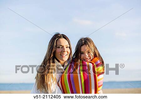 Stock Photography - Portrait of a mother embracing her daughter at the beach, smiling at camera. Fotosearch