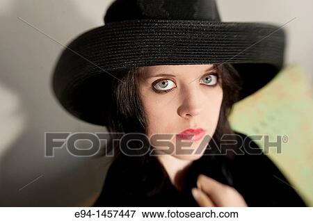 Stock Photo - Portrait of a nineteen year old brunette woman looking at the camera wearing a black hat. Fotosearch