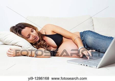 Portrait of a pregnant woman lying on a couch with a laptop in front of her View Large Photo Image Stock Photo - Portrait of a pregnant woman lying on a couch with a laptop in front of her. Fotosearch