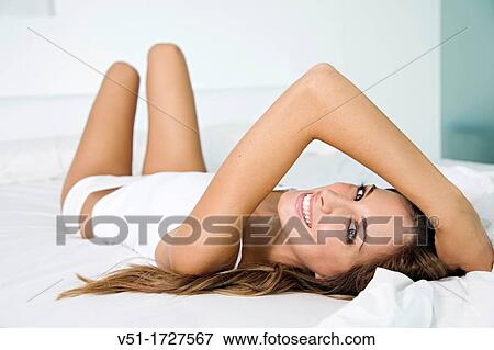 Stock Photo - Portrait of a pretty blonde woman smiling at camera in bed. Fotosearch