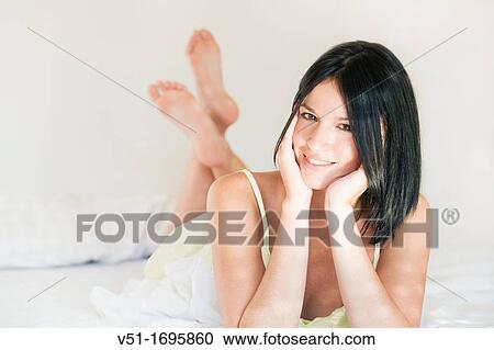 Portrait of a pretty brunette woman smiling at camera in bed View Large Photo Image Stock Image - Portrait of a pretty brunette woman smiling at camera in bed. Fotosearch