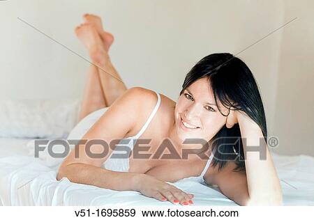 Stock Photo - Portrait of a pretty brunette woman smiling at camera in bed. Fotosearch