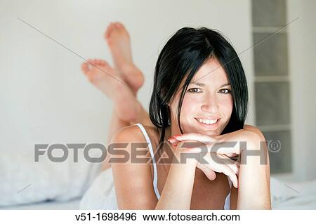 Stock Photograph - Portrait of a pretty brunette woman smiling in bed. Fotosearch