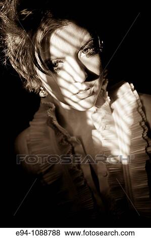 Stock Photo - Portrait of a redheaded woman looking at the camera with shadows on her face wearing a frilly blouse.. Fotosearch