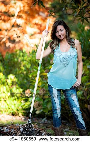 Portrait of a smiling 21 year old woman raking leaves in a garden setting View Large Photo Image Stock Photo - Portrait of a smiling 21 year old woman raking leaves in a garden setting. Fotosearch