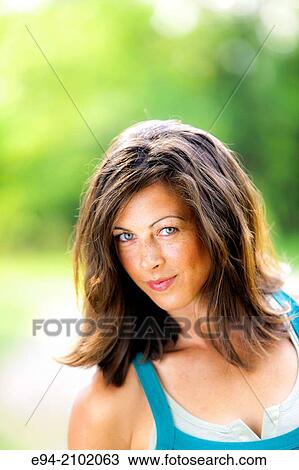 Stock Image - Portrait of a smiling 27 year old brunette woman looking at the camera, outdoors.. Fotosearch