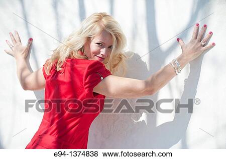 Portrait of a smiling 44 year old blond woman, outdoors looking over her shoulder with arms spread on to a white wall. View Large Photo Image Stock Photo - Portrait of a smiling 44 year old blond woman, outdoors looking over her shoulder with arms spread on to a white wall.. Fotosearch