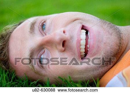 Stock Photo - Portrait of a smiling young man laying on grass. Fotosearch