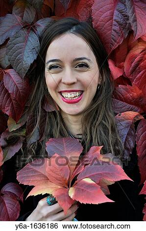 Stock Photograph - Portrait of a smiling young woman outdoors holding ivy leaf. Fotosearch