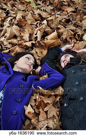 Portrait of a two young woman lying on autumn leaves from a bird's eye view laughing and having fun View Large Photo Image Stock Image - Portrait of a two young woman lying on autumn leaves from a bird's eye view laughing and having fun. Fotosearch