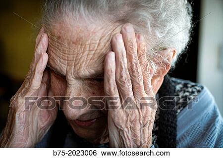 Stock Photograph - Portrait of a woman in a centennial elderly people home, with her hands at the temples and gesture of concern. Fotosearch