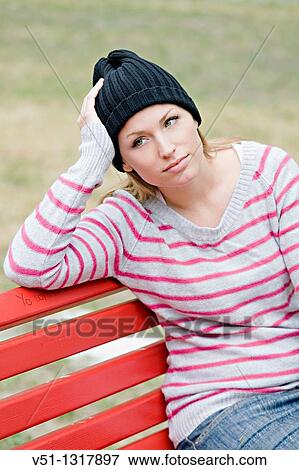 Stock Photo - Portrait of a woman sitting in a bench in the park in Autumn. Fotosearch