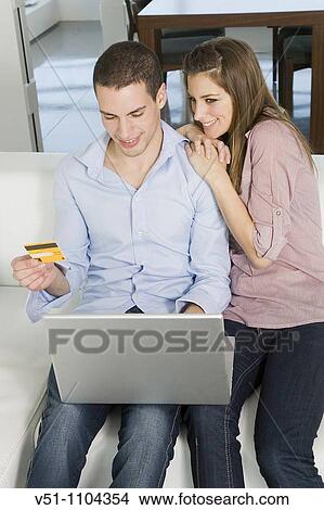 Picture - Portrait of a young couple buying with credit card in internet on the sofa. Fotosearch