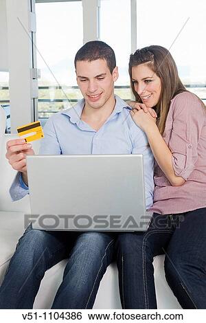 Portrait of a young couple on sofa using laptop and buying with credit card View Large Photo Image Stock Photograph - Portrait of a young couple on sofa using laptop and buying with credit card. Fotosearch