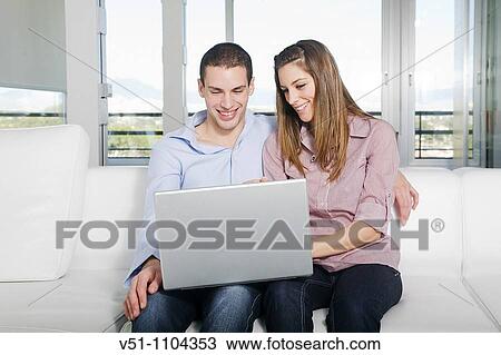 Stock Image - Portrait of a young couple sitting on the sofa using laptop. Fotosearch