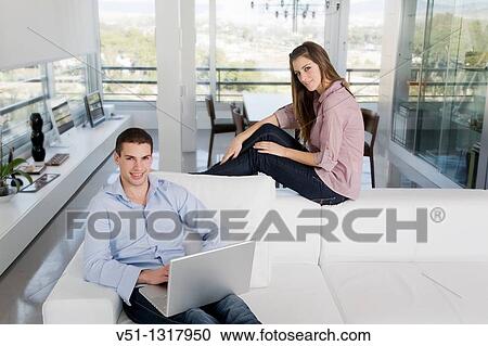 Portrait of a young couple sitting on the sofa using laptop View Large Photo Image Stock Image - Portrait of a young couple sitting on the sofa using laptop. Fotosearch