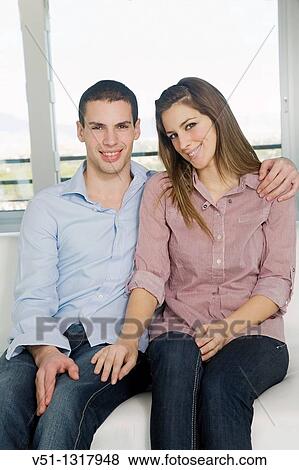 Portrait of a young couple sitting on the sofa and smiling at camera View Large Photo Image Stock Photo - Portrait of a young couple sitting on the sofa and smiling at camera. Fotosearch
