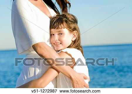 Portrait of a young girl embracing her mother at hte beach, smiling at camera View Large Photo Image Stock Photo - Portrait of a young girl embracing her mother at hte beach, smiling at camera. Fotosearch