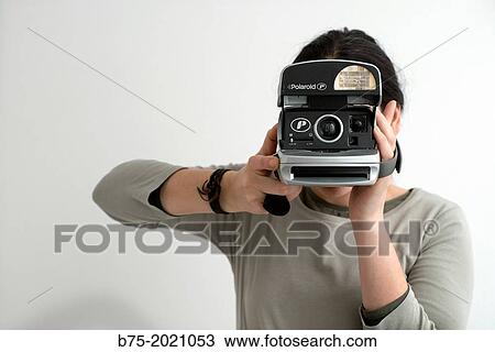 Stock Image - Portrait of a young girl taking a picture with a Polaroid camera. Fotosearch