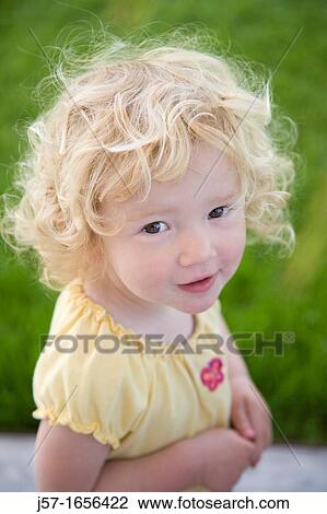 Stock Image - Portrait of a young girl with curly blond hair looking into the camera looking mischeivious. Fotosearch