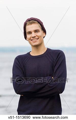 Stock Image - Portrait of a young man by the sea smiling at camera. Fotosearch