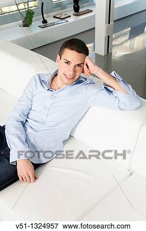 Portrait of a young man sitting on sofa and smiling at camera View Large Photo Image Stock Photo - Portrait of a young man sitting on sofa and smiling at camera. Fotosearch