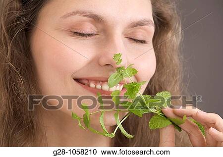 Stock Image - portrait of a young woman holding and smelling a sprig of mint. Fotosearch