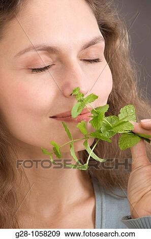Stock Photo - portrait of a young woman holding and smelling a sprig of mint. Fotosearch