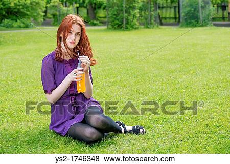 Portrait of a young woman sitting in a park with a bottle of orange soda View Large Photo Image Stock Photo - Portrait of a young woman sitting in a park with a bottle of orange soda. Fotosearch