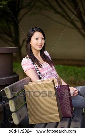 Portrait of a young woman sitting on a park bench with shopping bags View Large Photo Image Stock Image - Portrait of a young woman sitting on a park bench with shopping bags. Fotosearch