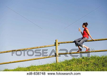 Portrait of a young woman sitting on a fence eating a ice cream View Large Photo Image Stock Photo - Portrait of a young woman sitting on a fence eating a ice cream. Fotosearch