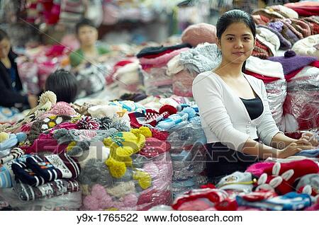 Portrait of a young woman standing next to piles of clothing at a market shop View Large Photo Image Stock Image - Portrait of a young woman standing next to piles of clothing at a market shop. Fotosearch