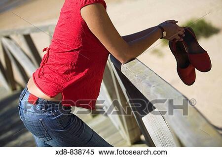 Stock Photography - Portrait of a young woman with a pair of sandals on the beach. Fotosearch