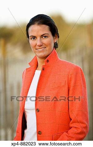 Stock Image - Portrait of a young woman with brown hair tied behind her ears wearing a pink jacket with collar and white shirt.. Fotosearch