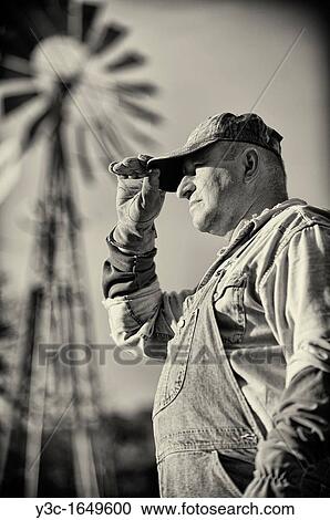 Stock Image - Portrait of American Farmer Vintage Style Black and White with Ranch Windmill in Background. Fotosearch