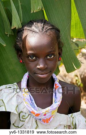 Stock Photo - Portrait of an African girl with white spots on her face looking at the lens with banana leafs as background, Tanji Village, Tanji, Gambia, Africa. Fotosearch
