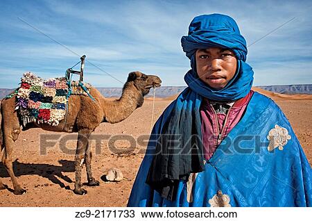 Stock Image - Portrait of Berber boy with his camel in Tinfou dunes near Tamegrout, Zagora, Draa Valley, Morocco. Fotosearch